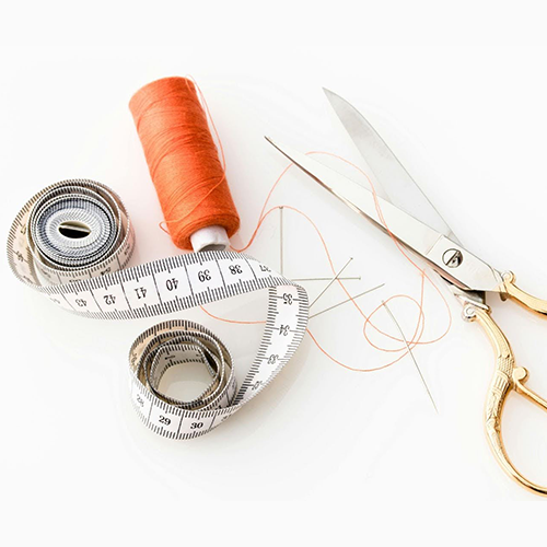 a neutral cream background with a measuring tape, orange spool of thread and scissors with gold handle and silver shears