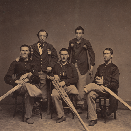 the image shows 5 civil war soliers, the front 3 are seated showing off missing limbs, mostly legs with their wooden crutches across their laps