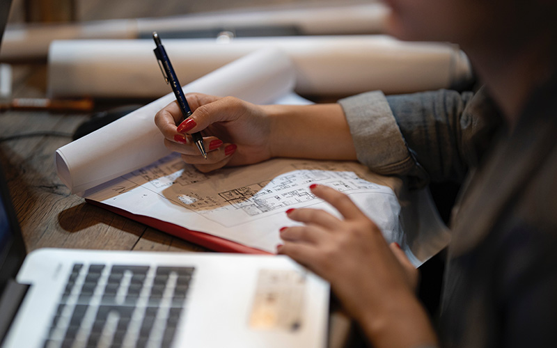 A young woman with an open laptop taking notes. The focus is on her hands and the notepad.