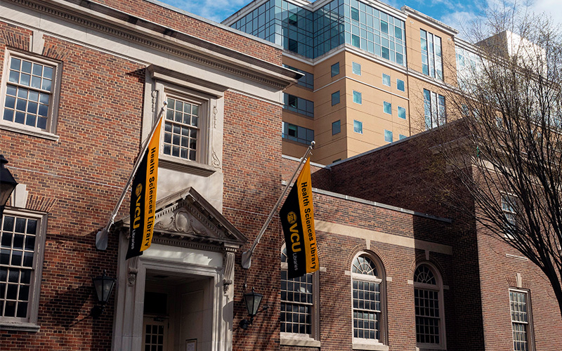 The Health Sciences Library facade with flags stating Health Sciences Library in VCU Gold and black.
