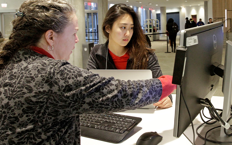 Teresa Doherty of VCU Libraries helps a student on the computer at the Information Desk at James Branch Cabell Library.