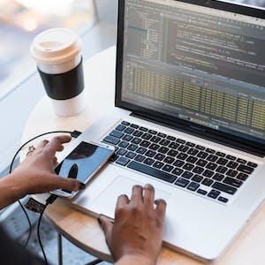 Female researcher's hands on a laptop keyboard and phone, with a coffee in the background
