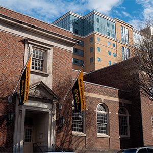 an image of a brick building with two black and gold flags out front against a blue sky