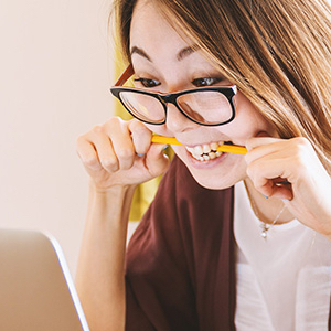 Woman biting pencil in frustration as she looks at computer screen