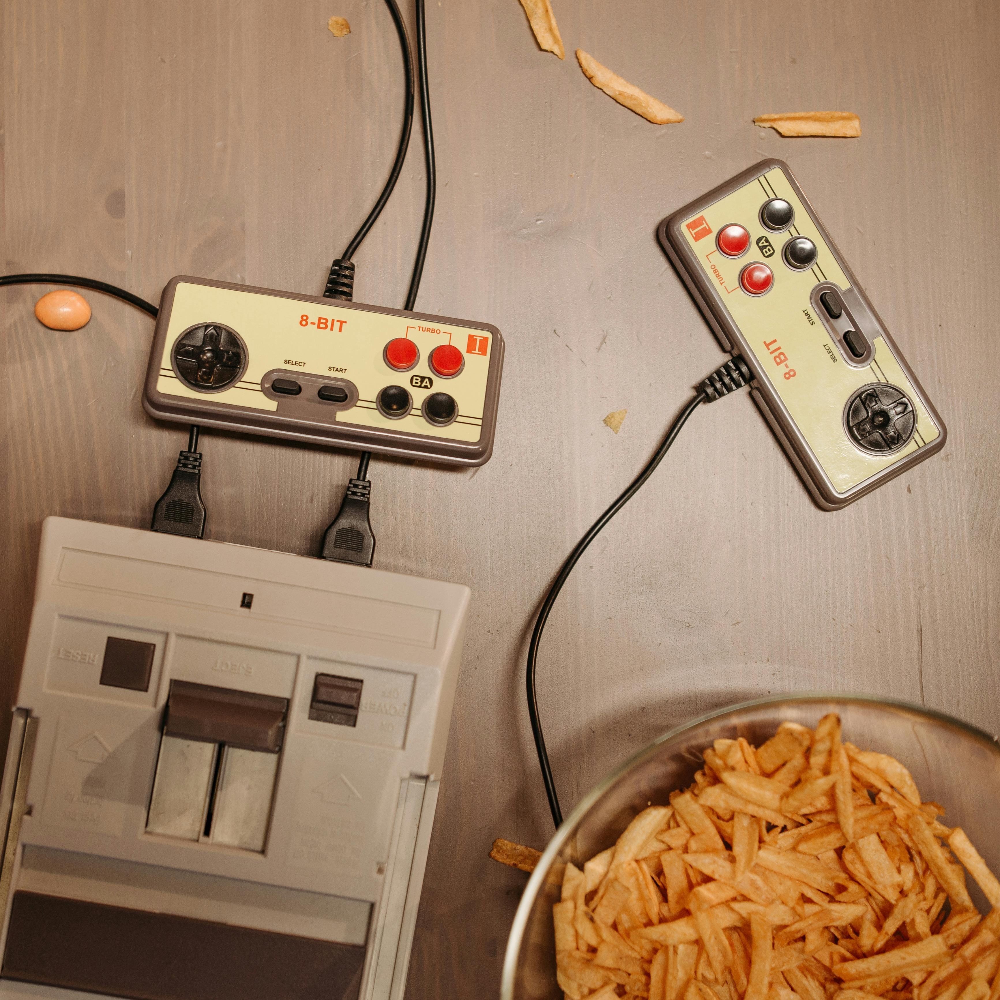 The image shows an old school gaming system with two controlers plugged in and a bowl of french fries in the bottom right corner
