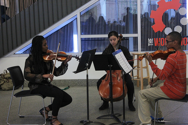 Three VCU undergraduate students perform classical music beside the first-floor main staircase of James Branch Cabell Library.
