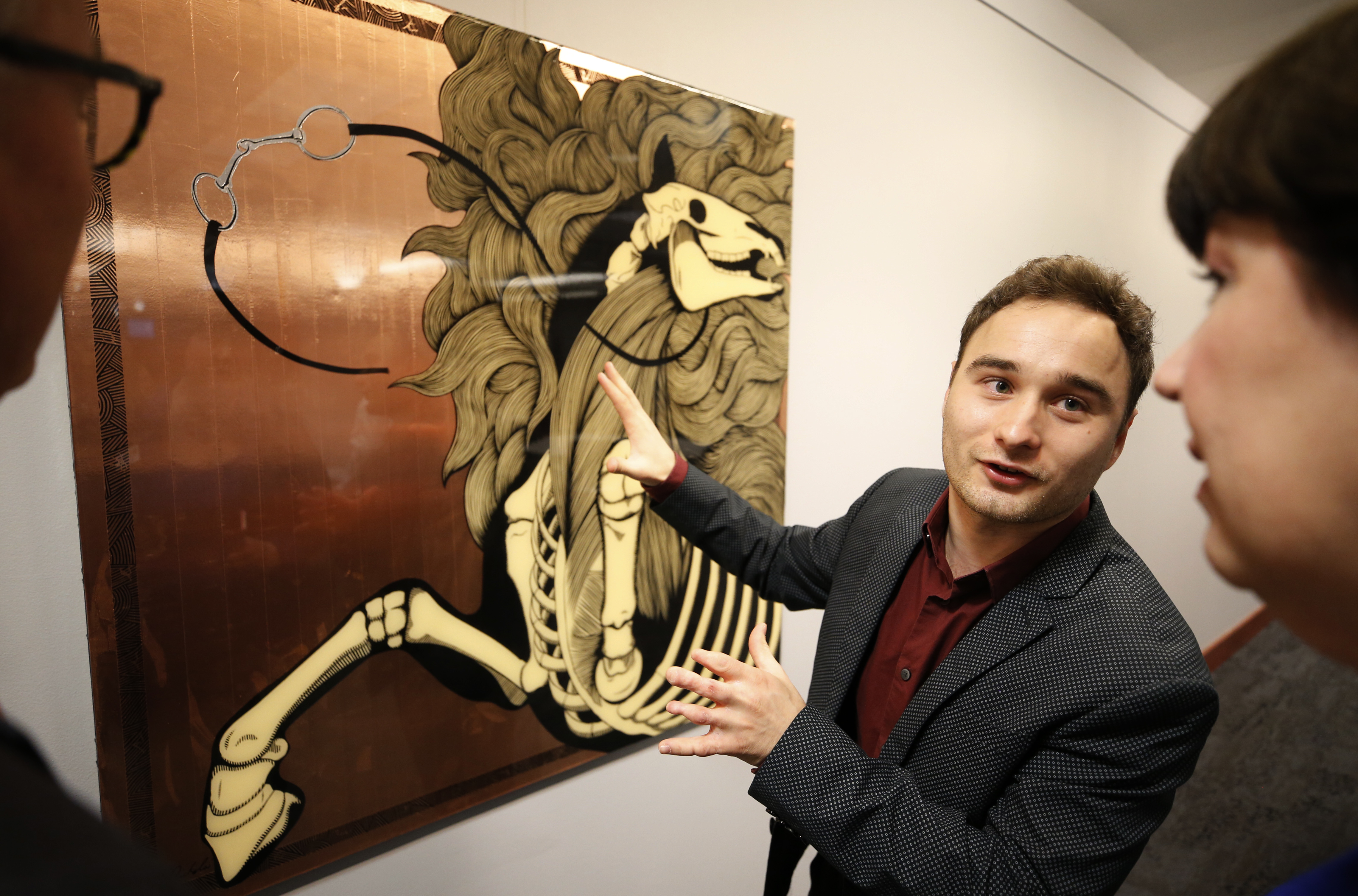 Artist Nickolai Walko gesturing at a piece of his depicting a horse with the skeleton exposed