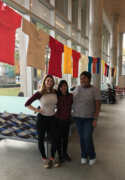 Three students from SAVES standing in front of the Clothesline Project in Cabell Library.