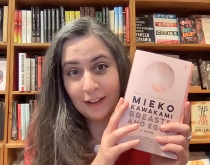 Kelly Justice holding up a copy of Breasts and Eggs by Mieko Kawakami on Zoom