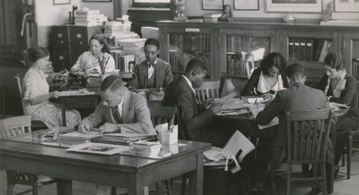 An old photo of people in a public library at desks reading.