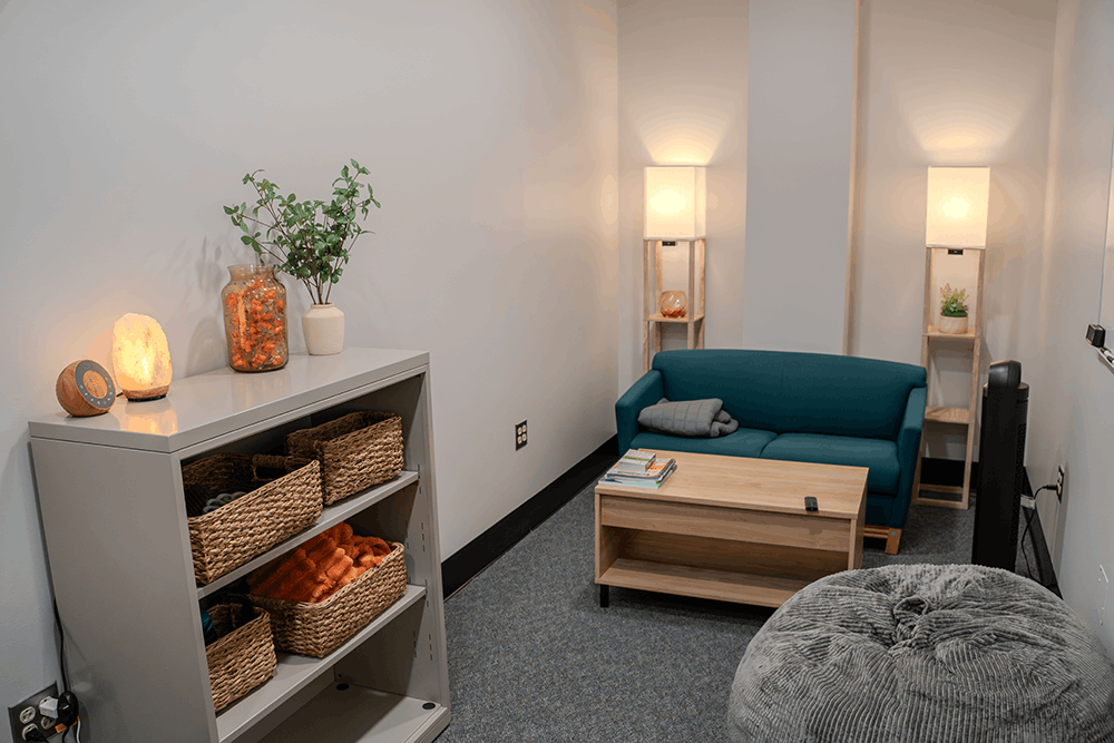 A small room with 2 floor lamps, a sofa, and a bookshelf